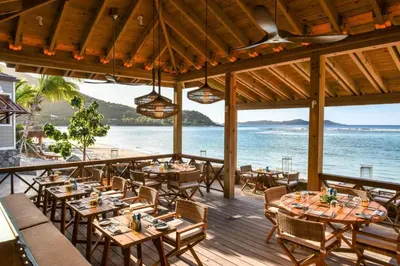 a restaurant on the beach with tables and chairs at Rosewood Little Dix Bay in Virgin Gorda Airport