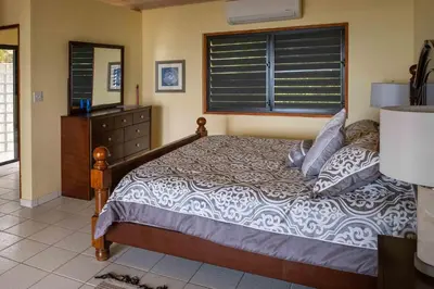 a bedroom with a bed with a dresser and a window at Villa ValMarc Mahoe Bay Virgin Gorda BVI in Virgin Gorda