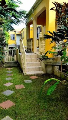 a yellow house with a porch and stairs in the yard at SUNFLOWER LANE QUEEN Balcony Room APARTMENT in Tortola Island