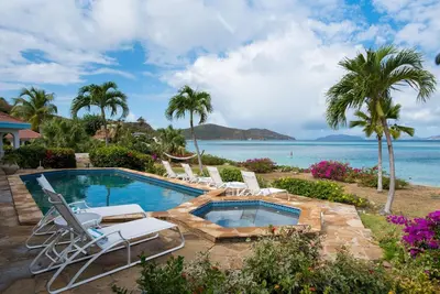a swimming pool with lounge chairs and the ocean at BEACH DREAMS in Virgin Gorda