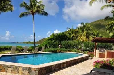 a swimming pool with chairs and the ocean in the background at CARIBBEAN WIND in Virgin Gorda