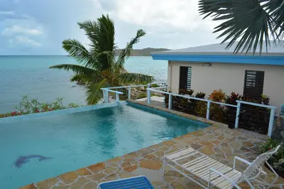 a swimming pool next to a house and the ocean at SERENDIPITY in Virgin Gorda