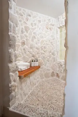 a bathroom with a stone wall and a wooden shelf at Long Bay Beach Resort in Tortola Island